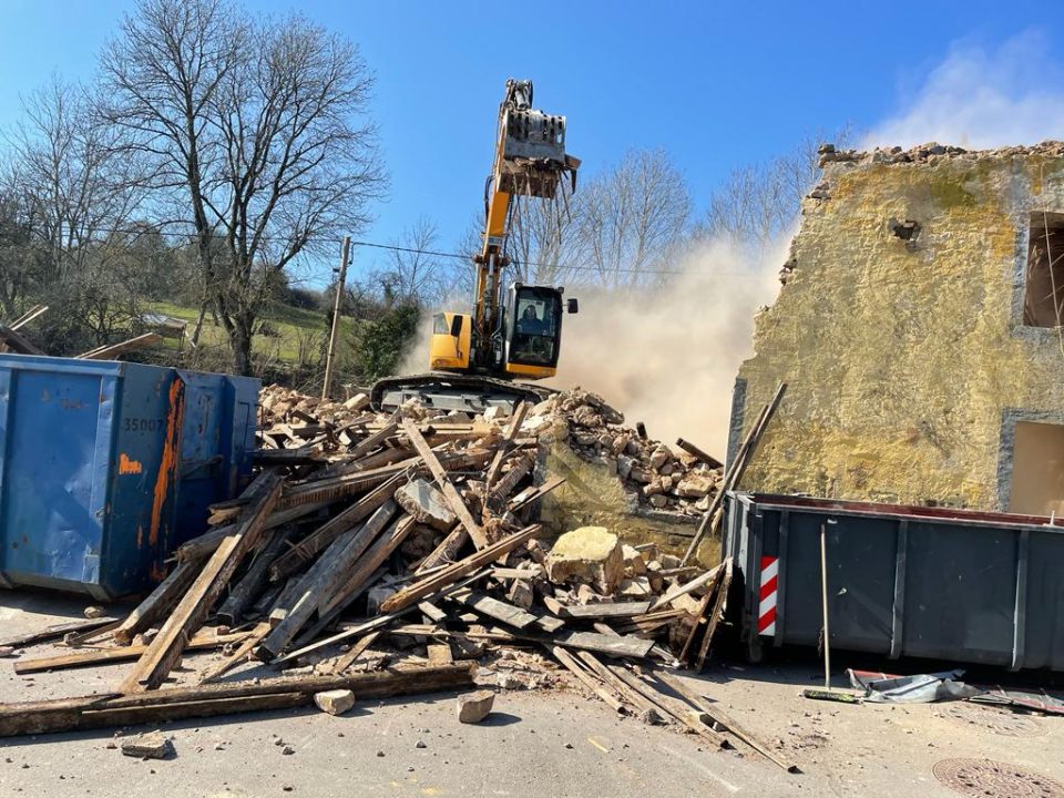 Abbruchbagger vor einem teilabgebrochenen Bruchsteinhaus
